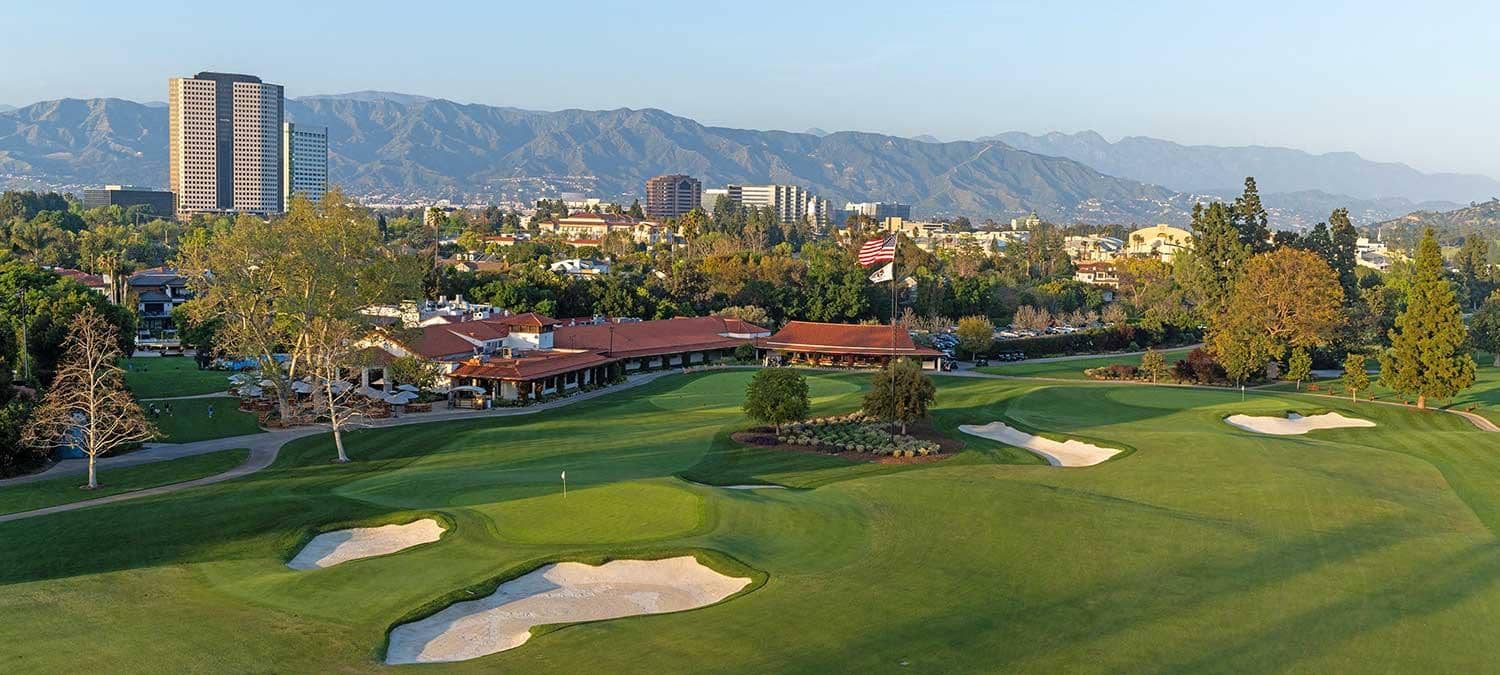 Photo courtesy of Lakeside Golf Club (lakesidegolfclub.com), used for editorial coverage. The Spanish-style clubhouse and closing green with Universal City and the San Gabriel Mountains in the distance.