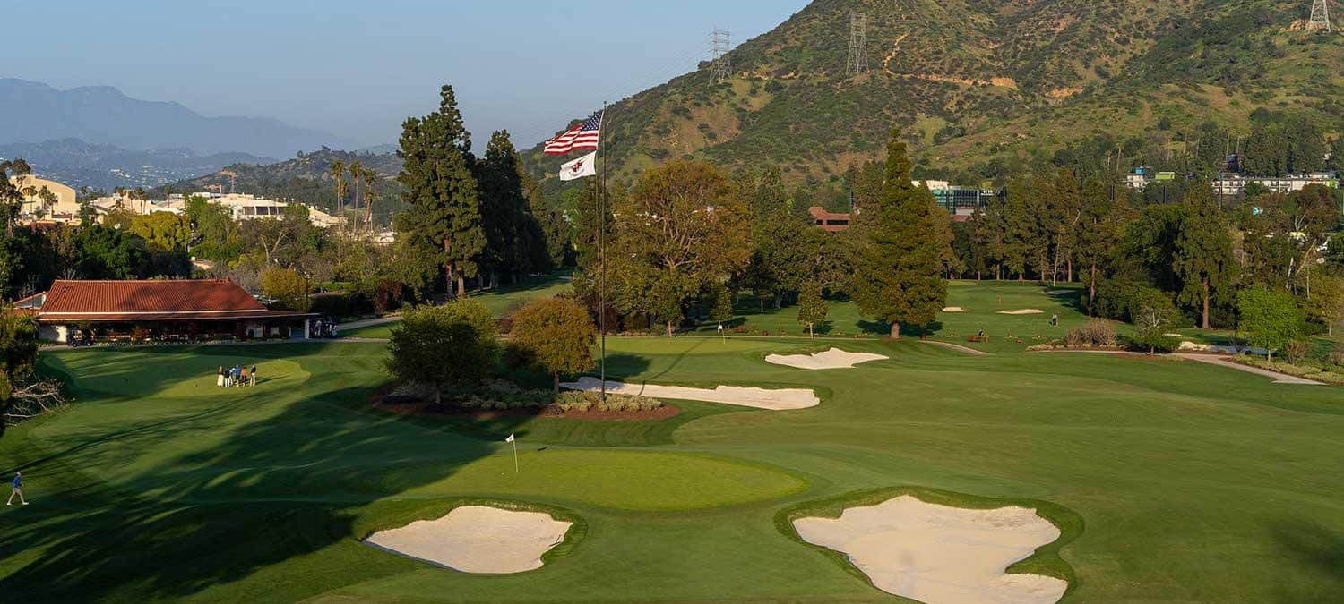 Photo courtesy of Lakeside Golf Club (lakesidegolfclub.com), used for editorial coverage. Green complex, bunkers, clubhouse and flagpole framed by the Verdugo Mountains.
