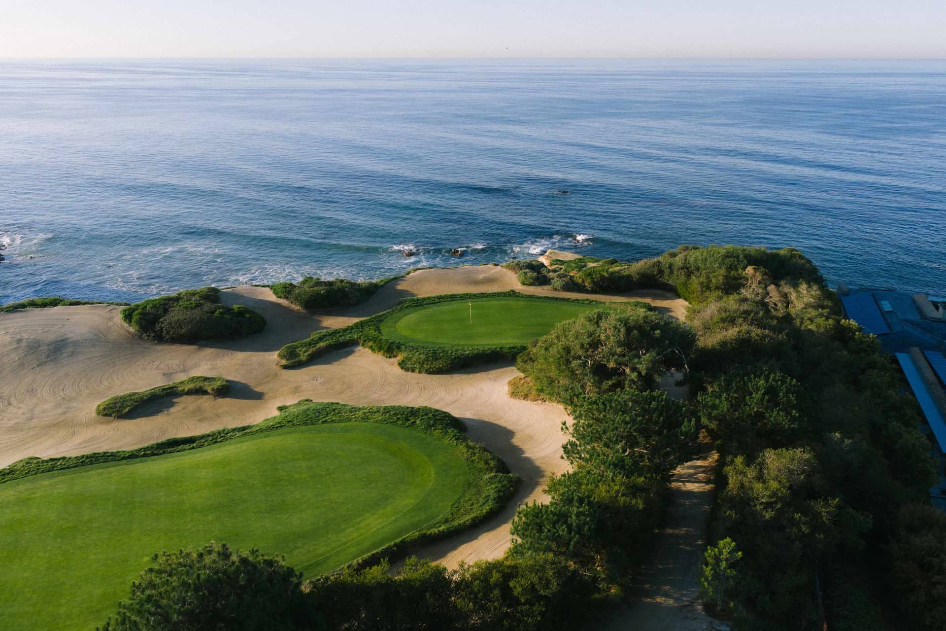 Two greens and the dune-like sand feature beside the ocean at Pelican Hill Ocean South hole 13.