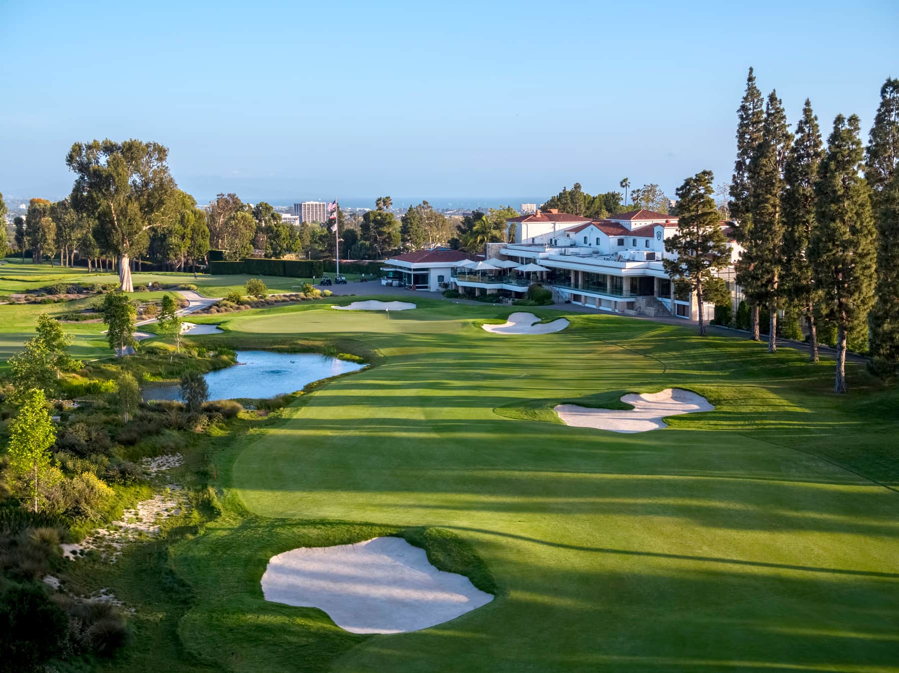 Brentwood Country Club, Los Angeles - view of the Spanish-style clubhouse across the closing hole, bunkers and pond. Credit: Origins Golf Design (Todd Eckenrode), originsgolfdesign.com. Used for editorial coverage on a non-commercial site.